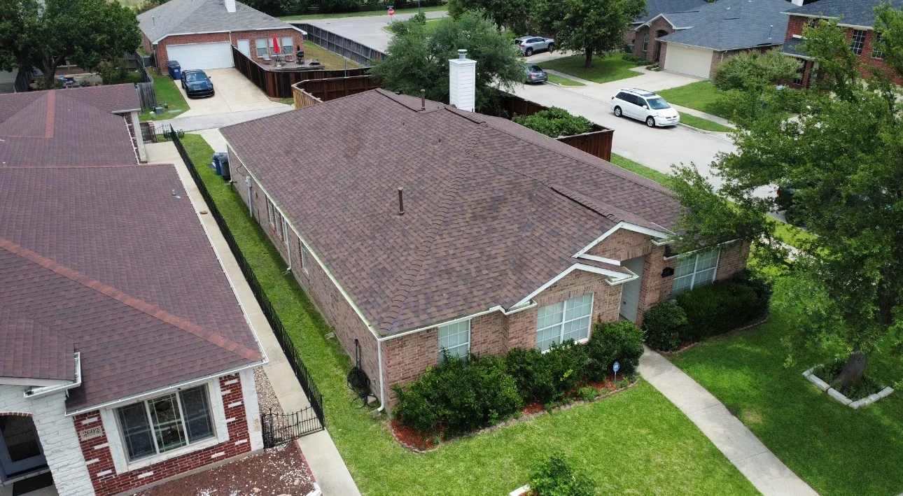 Aerial view of newly installed gray architectural shingle roof on brick home with white gutters