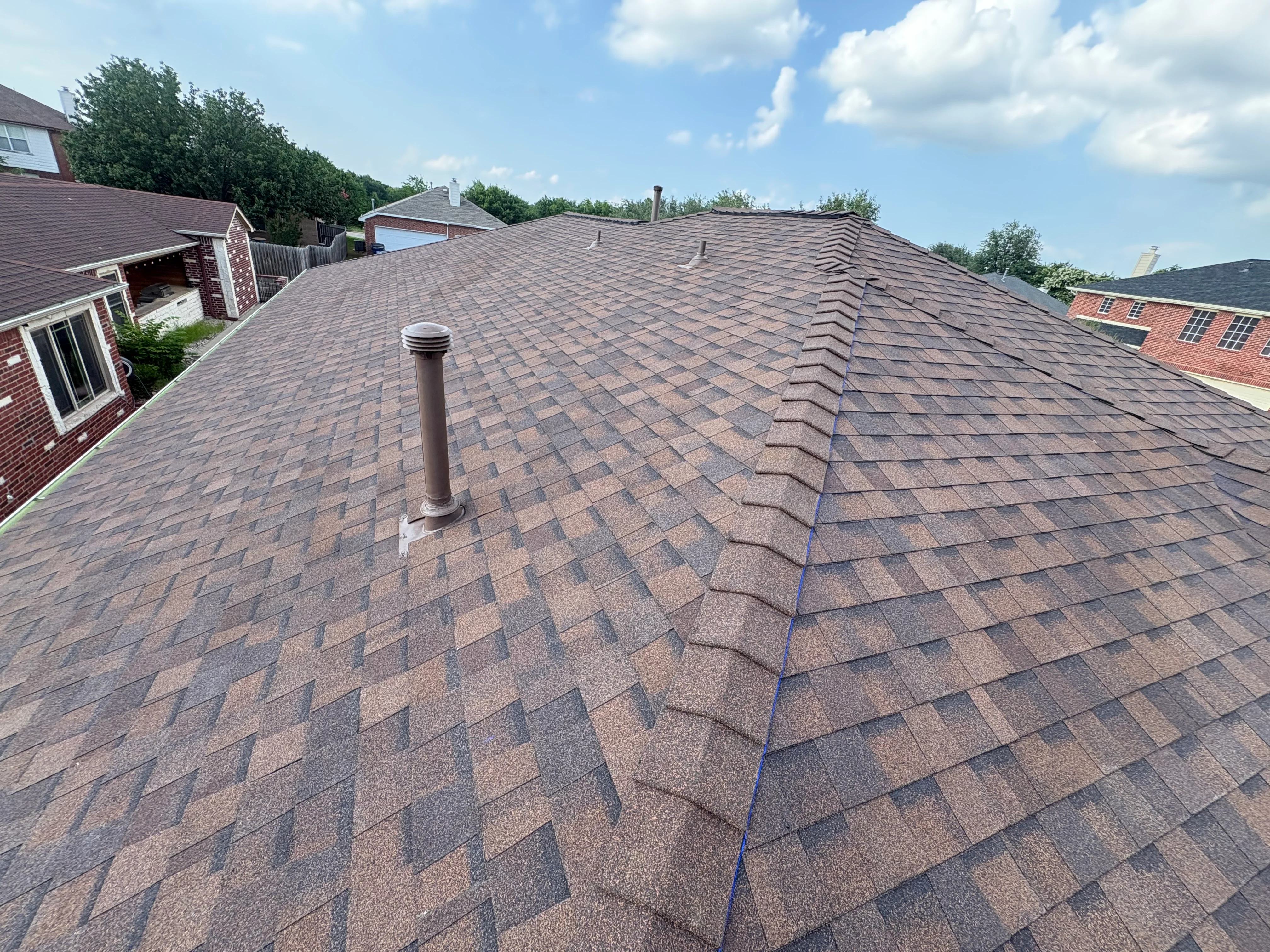 Newly installed architectural shingle roof with brown tones and proper ridge alignment on residential home