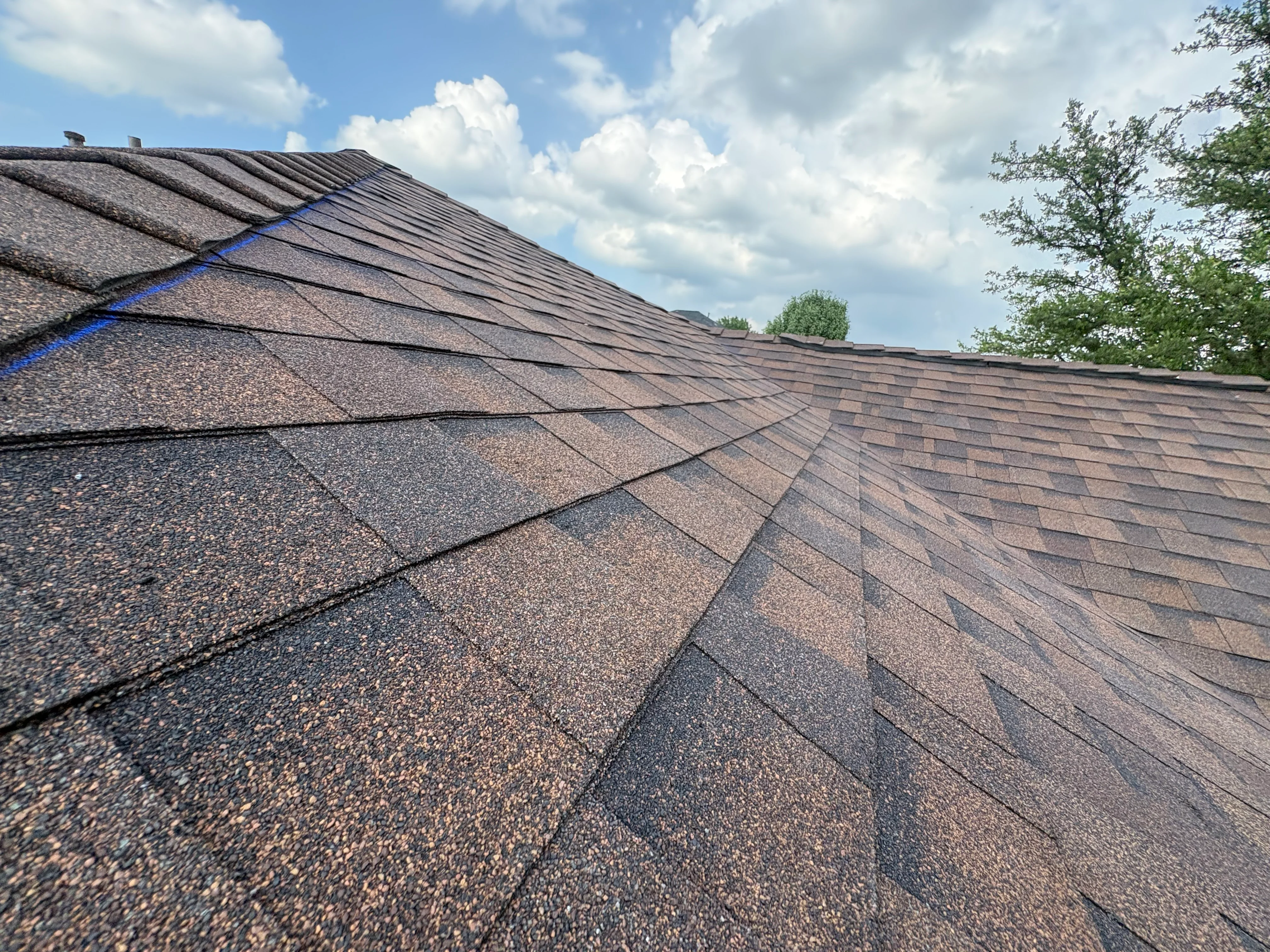 Newly installed architectural shingle roof with charcoal and brown tones showing proper alignment and ridge caps