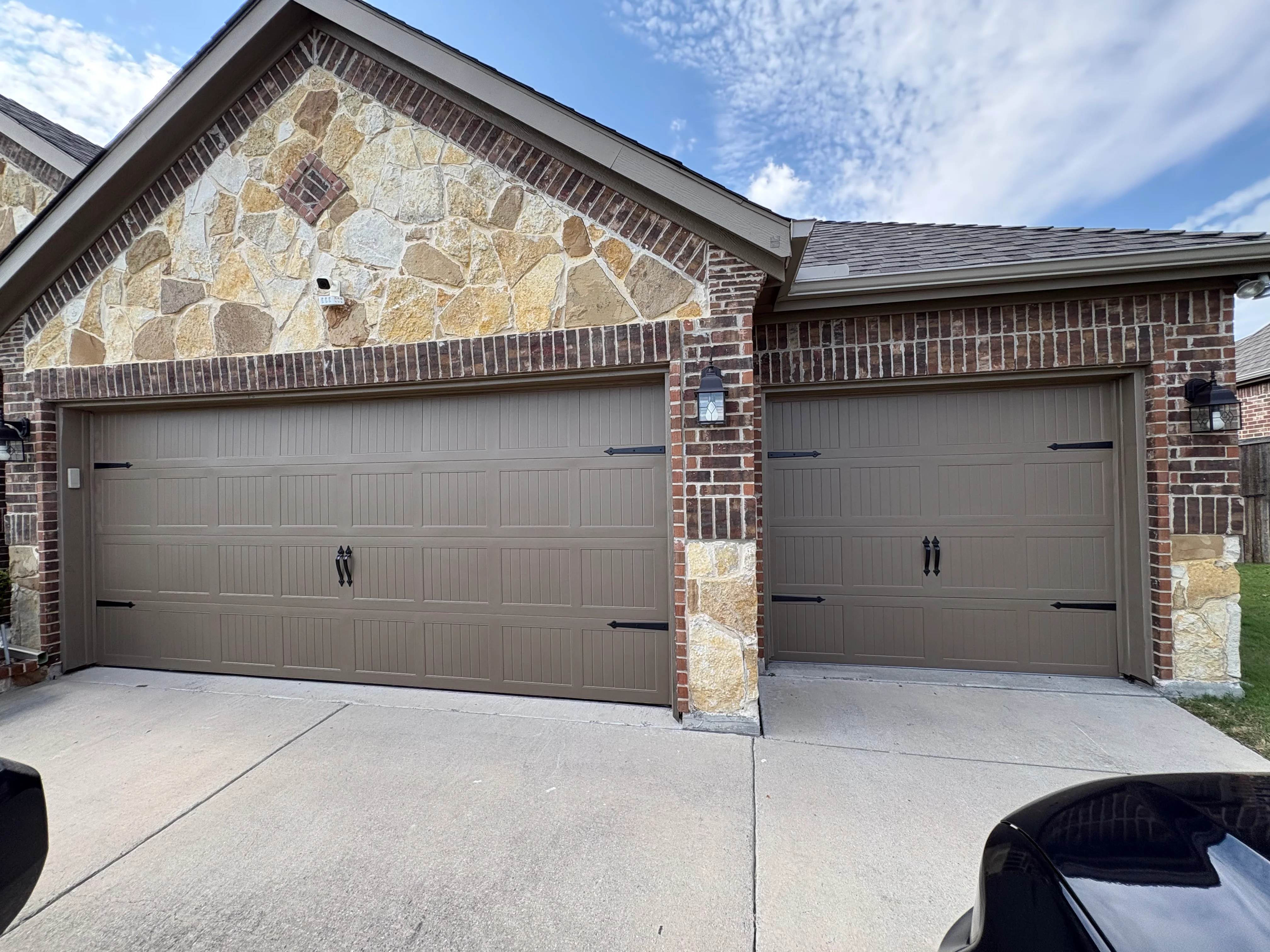 Two tan garage doors with black hardware on brick and stone veneer home exterior