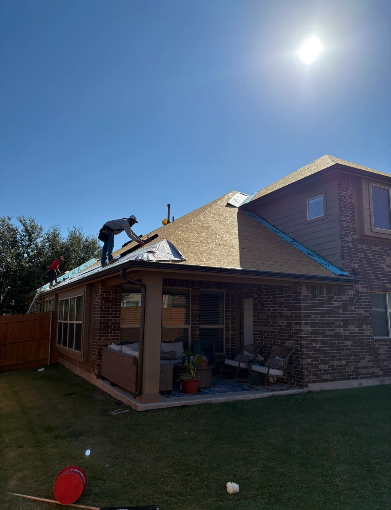 Roofers installing new asphalt shingles on brick residential home with patio