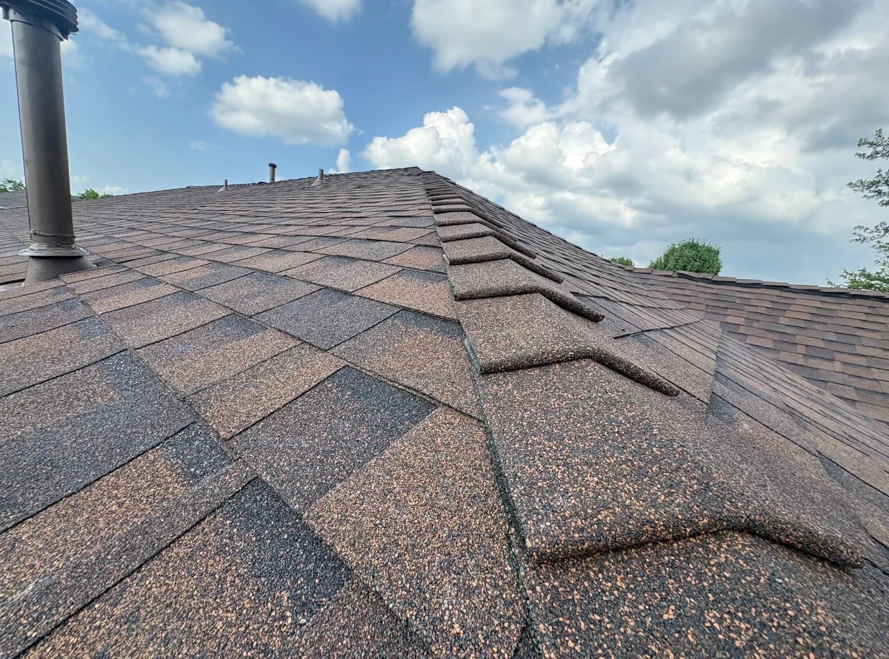 New architectural shingle roof with brown and gray tones, ridge vents, and metal chimney flashing