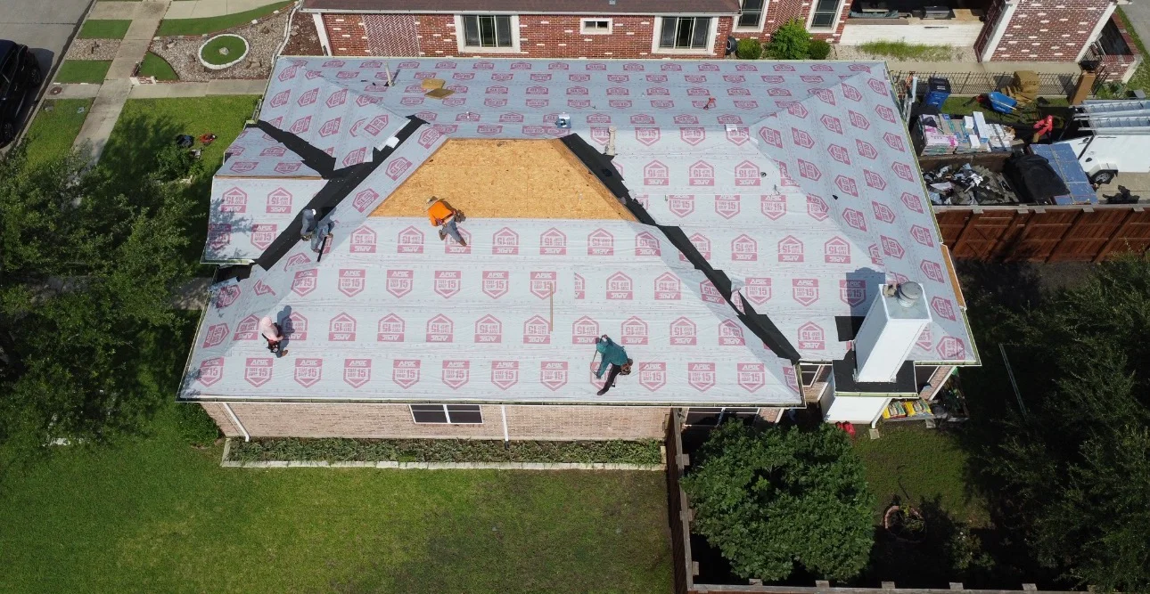 Aerial view of residential roof replacement with workers installing underlayment and sheathing