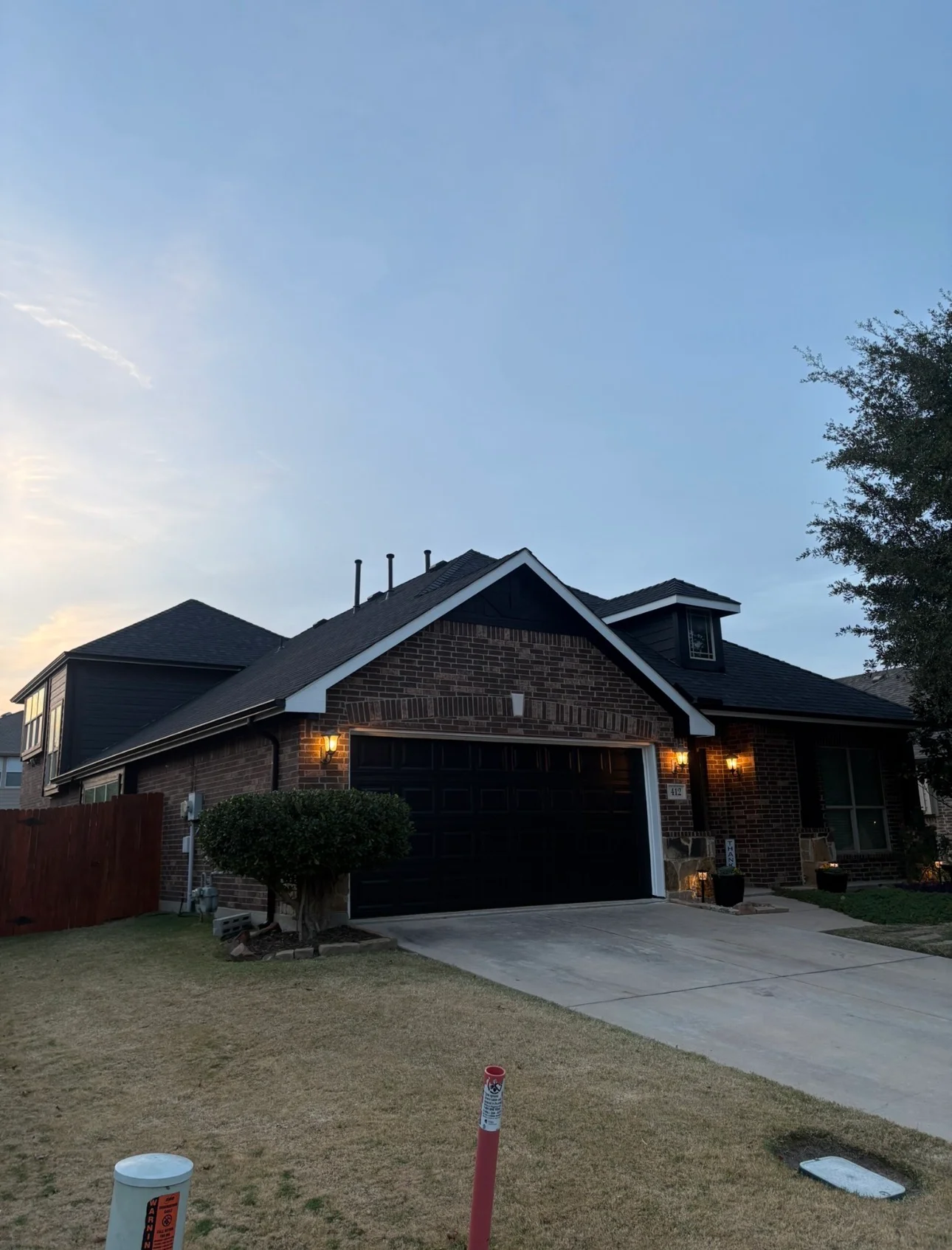 Two-story brick home with newly installed dark shingle roof and white trim at dusk