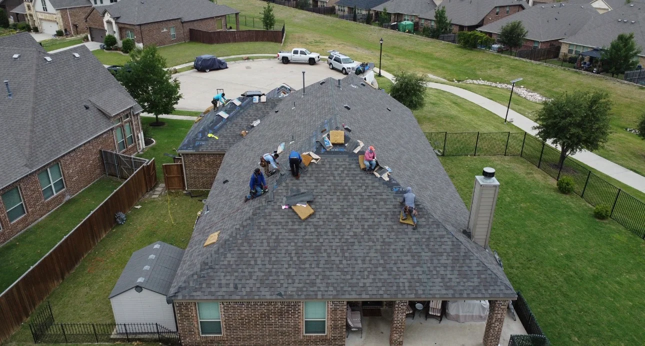 Aerial view of residential roof replacement in progress with crew installing gray architectural shingles