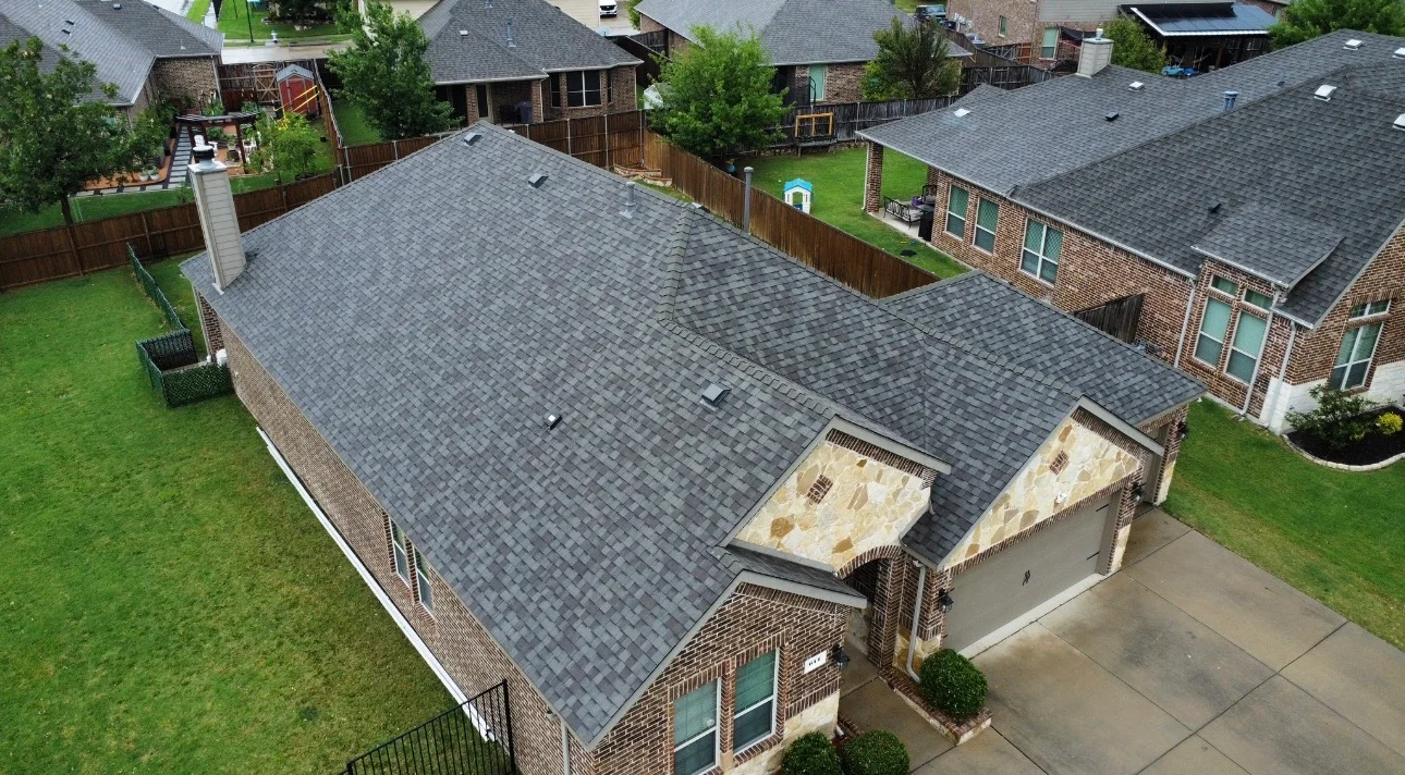 Aerial view of brick home with new charcoal gray asphalt shingle roof and stone dormers