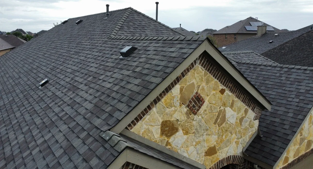 New gray architectural shingle roof with stone chimney and dormers on residential home