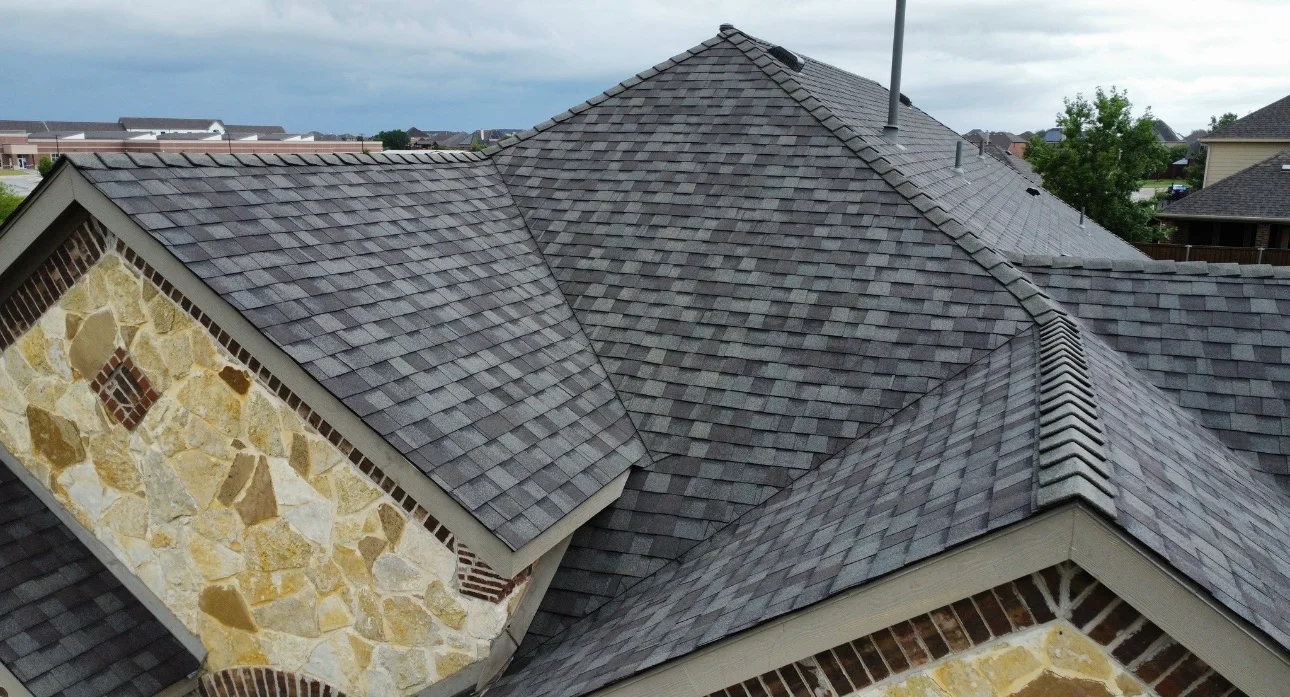 Charcoal gray architectural shingle roof with multiple peaks and stone chimney on residential home