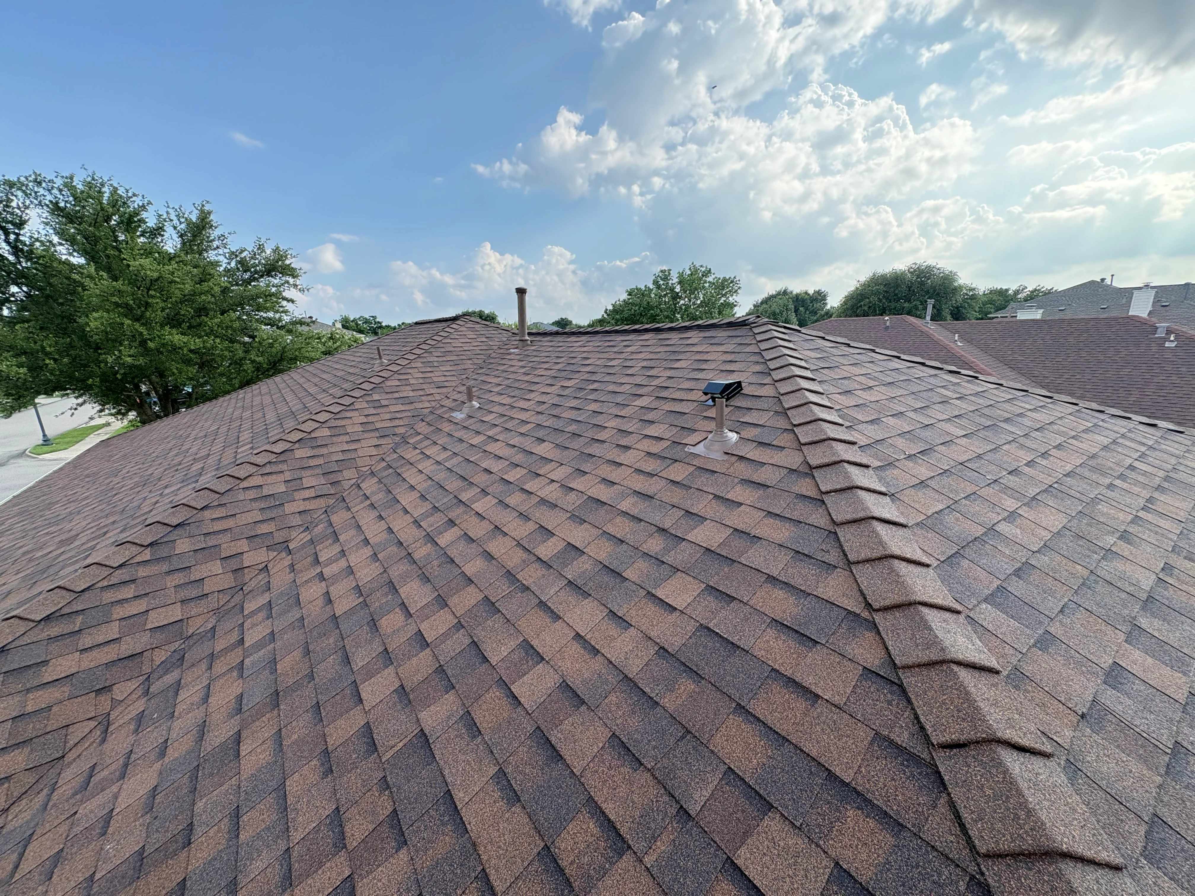 Newly installed brown architectural shingle roof with ridge caps and roof vent on residential home